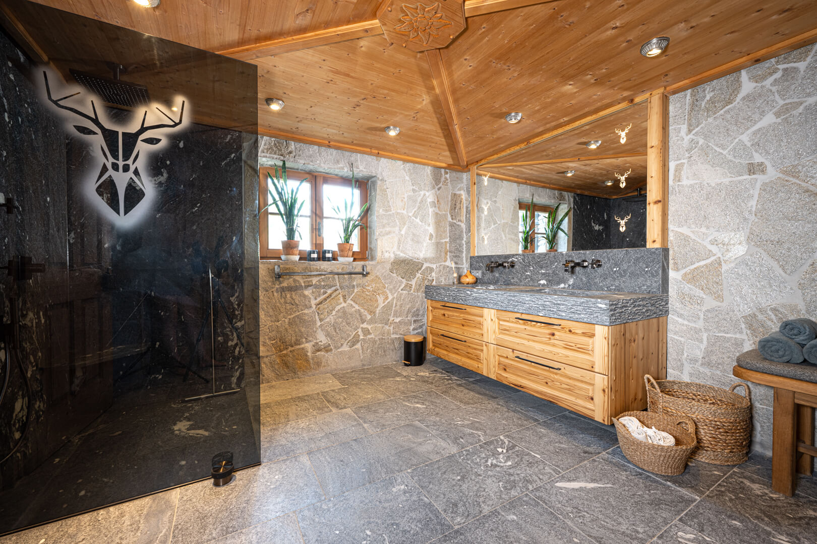 Alpine chalet bathroom featuring gray glass shower wall, natural stone, and reclaimed oak.