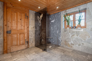 Chalet bathroom with stone shower, dark shower wall, and oak door.
