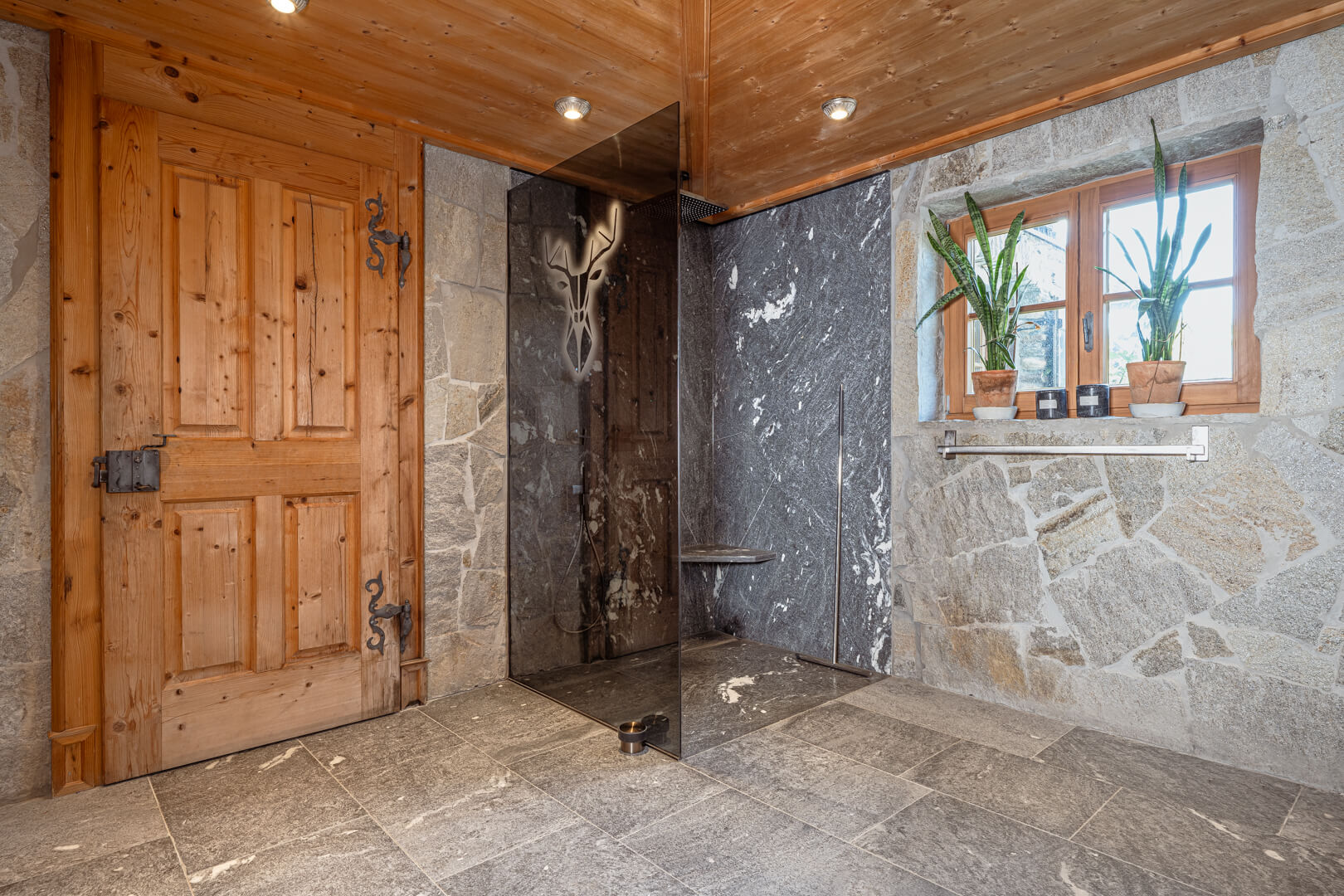 Chalet bathroom with stone shower, dark shower wall, and oak door.