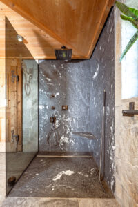 Alpine chalet shower with gray wall, natural stone, and oak details.
