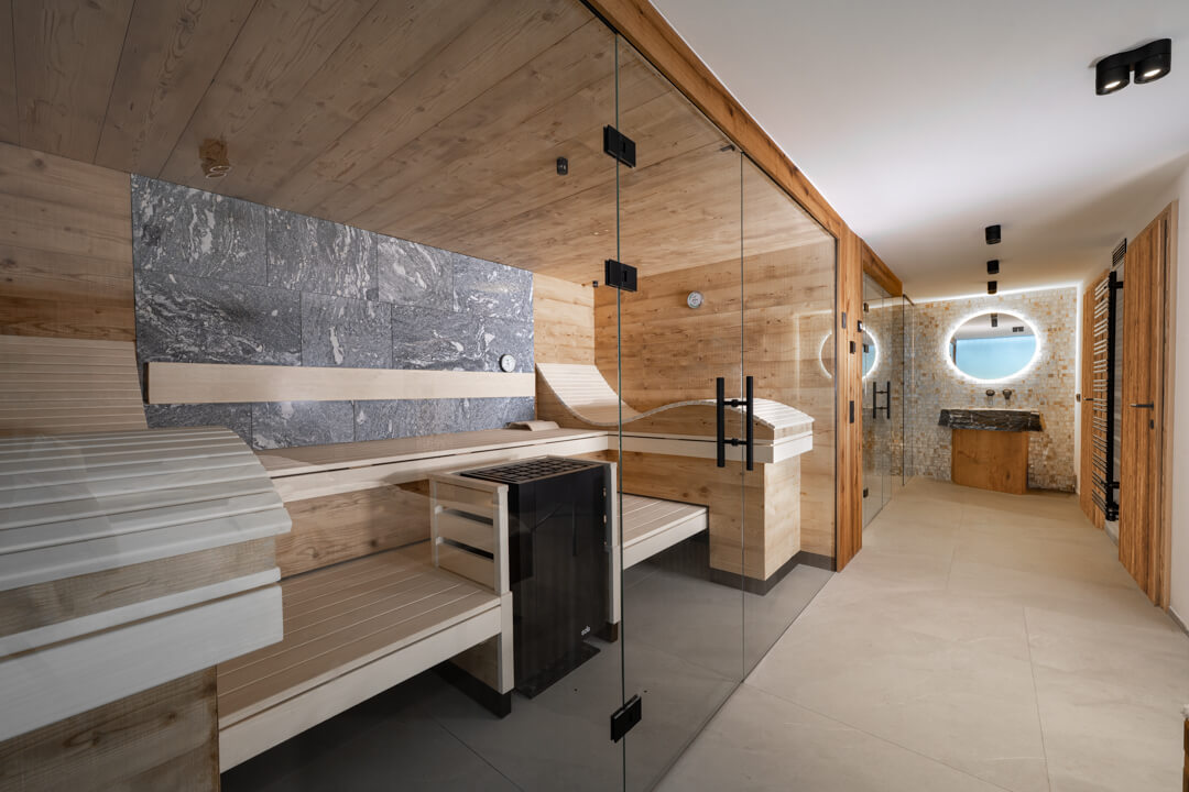 Reclaimed spruce sauna with gray natural stone, steam sauna, and black walk-in rain shower with mother-of-pearl tiles.