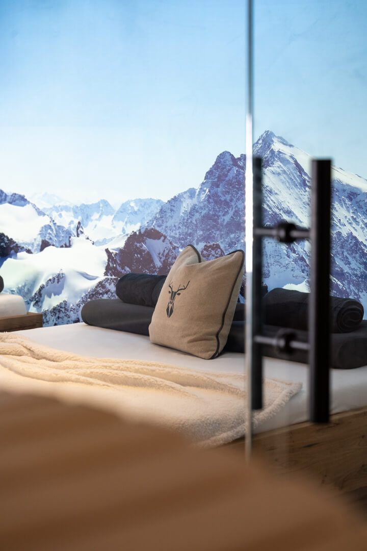Wellness relax bed made of oak with linen deer-motif cushions and winter mountain photo canvas.