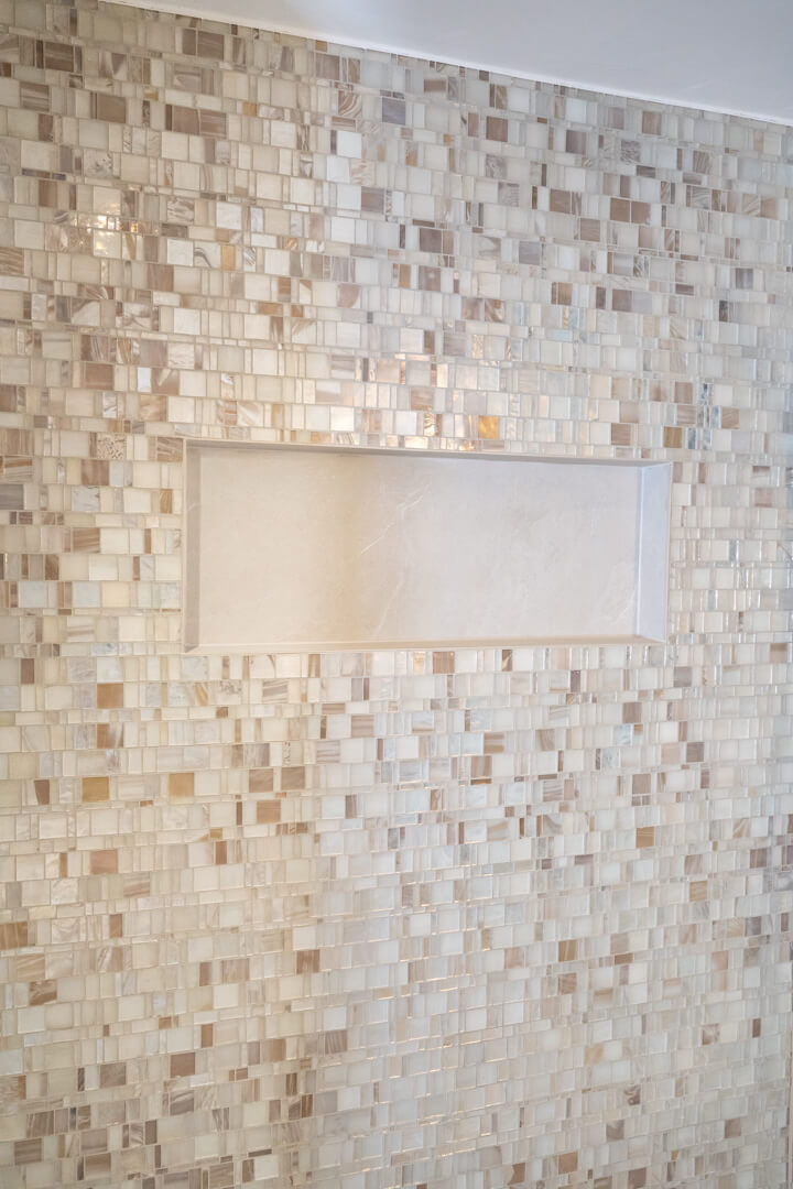 Shower wall with mother-of-pearl tiles and stone niche in chalet bathroom.
