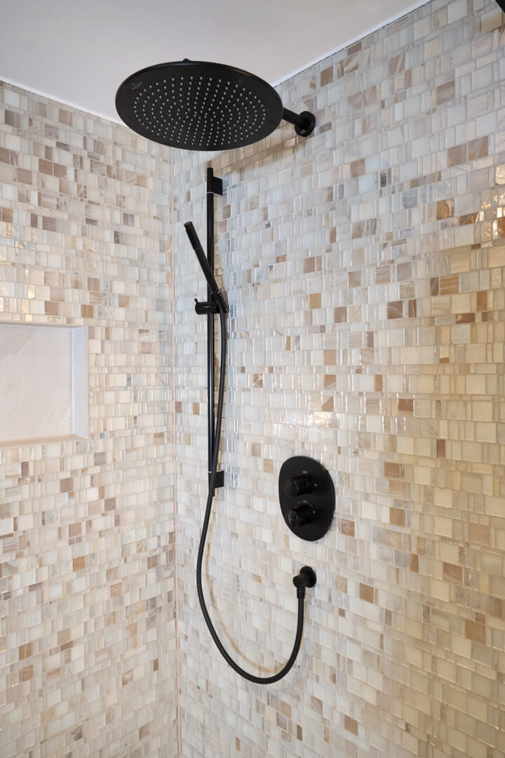 Chalet bathroom shower wall with mother-of-pearl tiles, stone niche, and black rain shower.