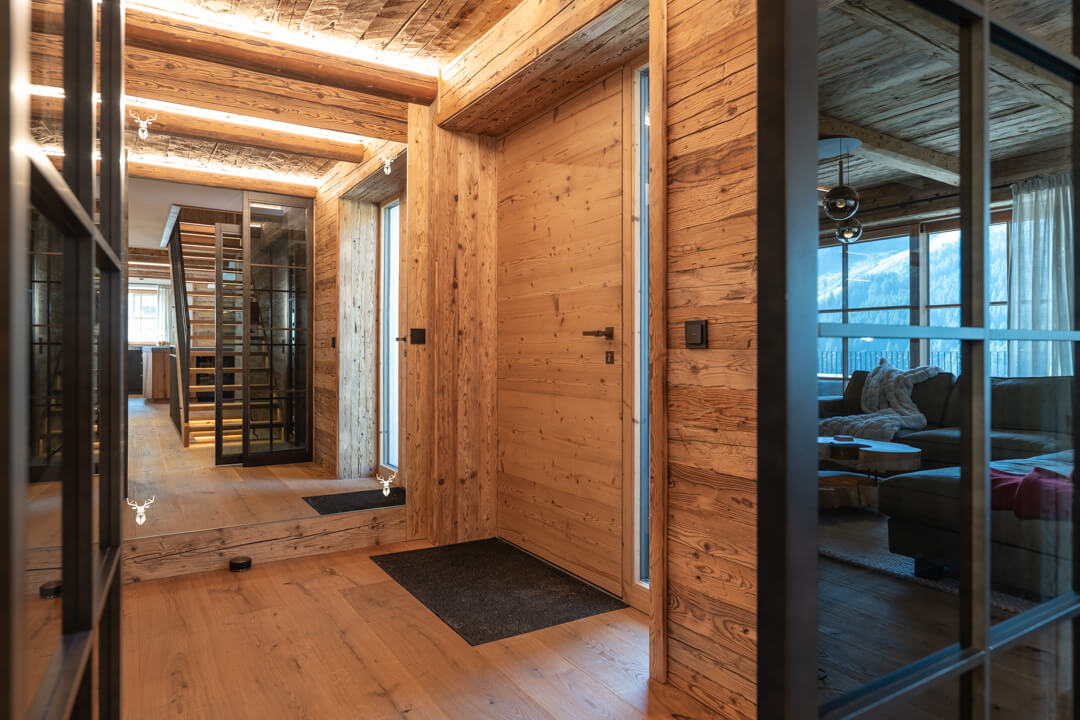 Chalet entrance with reclaimed wood, loft-style doors, mirror, and illuminated deer motifs.