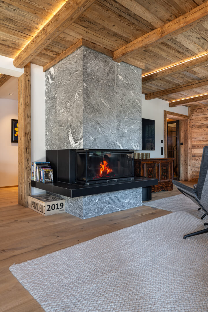 Chalet living room with massive Rauriser natural stone fireplace, reclaimed wood ceiling, and white wool rug.