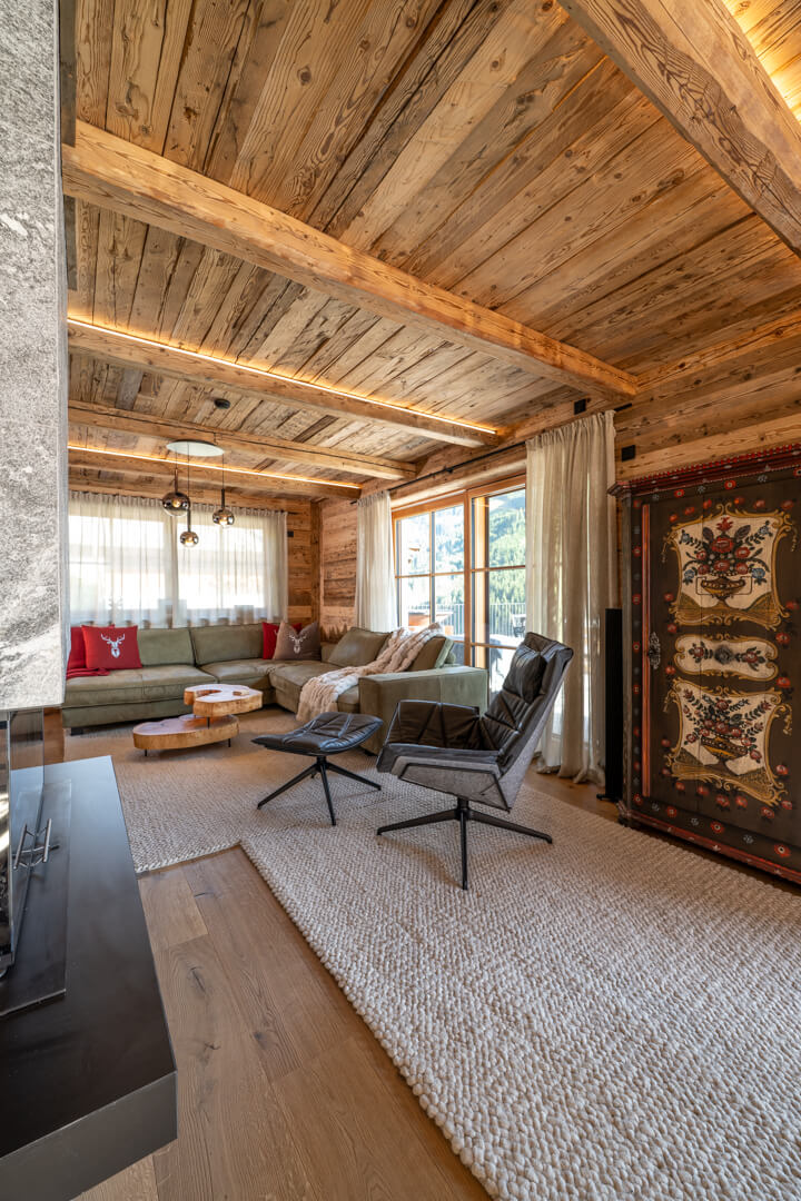Alpine living room with ash burl coffee table, white wool felt rug, green leather sofa, leather armchair, and illuminated reclaimed wood ceiling.