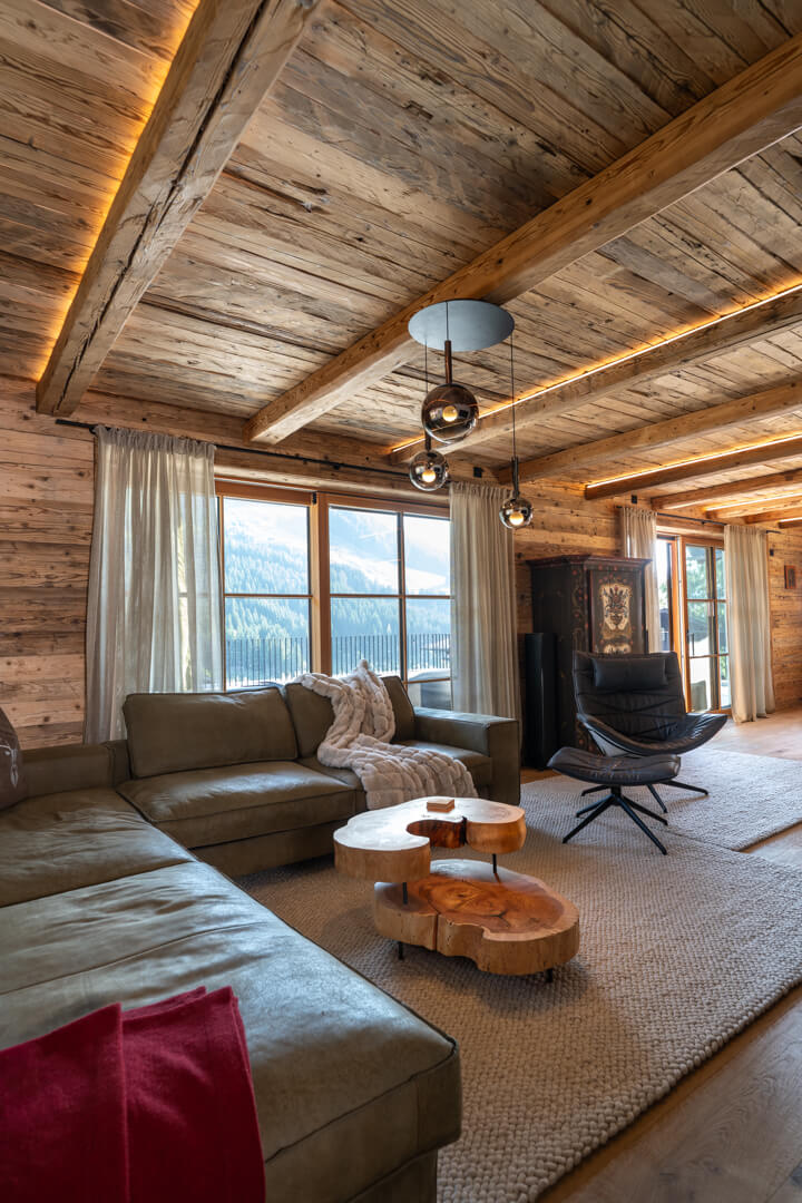 Alpine living room with ash burl coffee table, green leather sofa, leather armchair, and illuminated reclaimed wood ceiling.