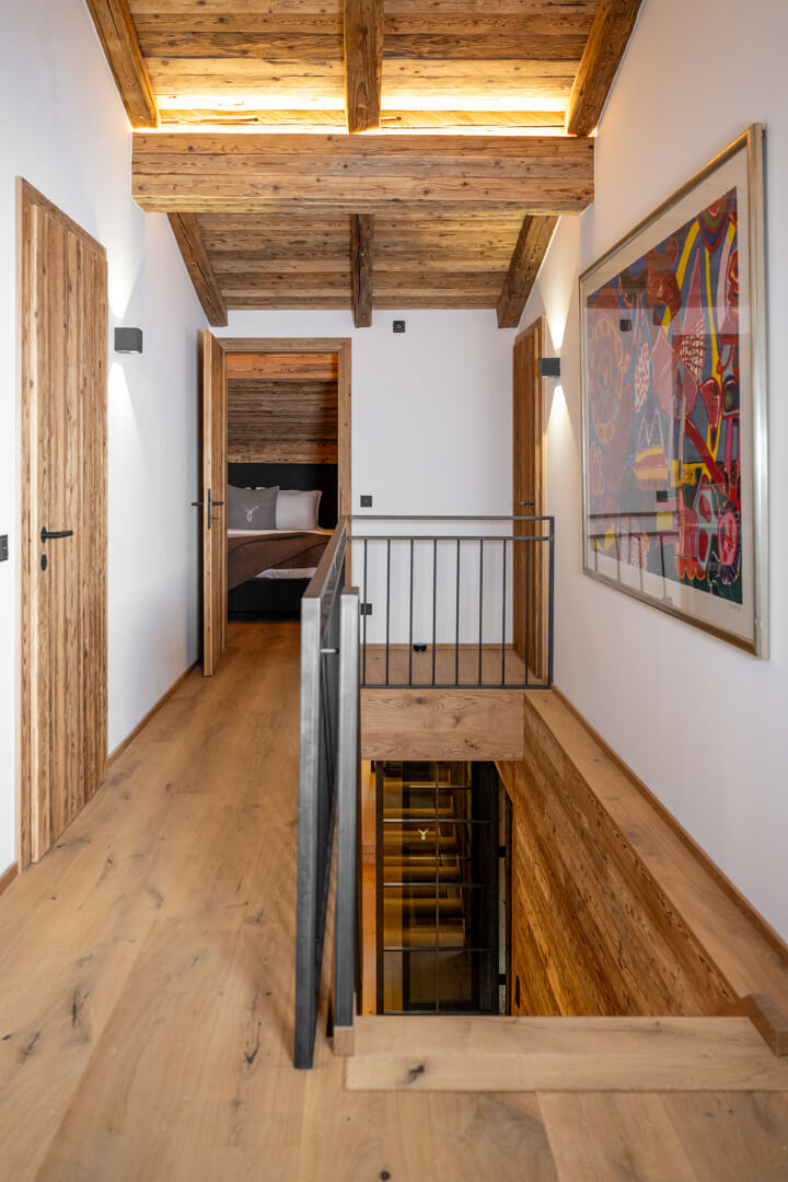 Chalet staircase with oak plank flooring, steel railing, and reclaimed wood ceiling.