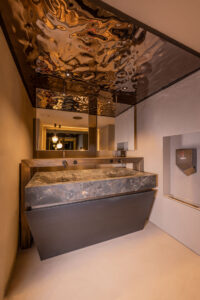 Luxury bathroom with solid stone sink, copper fixtures, and mirrored ceiling.