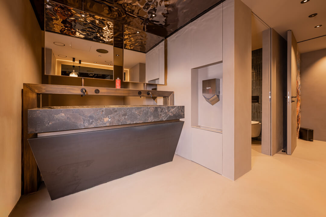 Luxury bathroom with bronze furniture, solid stone sink, copper fixtures, mirrored ceiling. Toilet with small green tile wall.