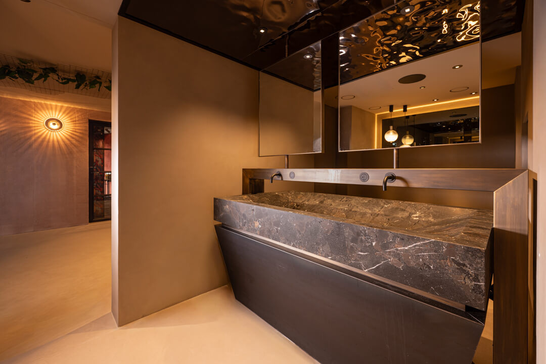 Luxury bathroom with solid stone sink, copper fixtures, and mirrored ceiling.