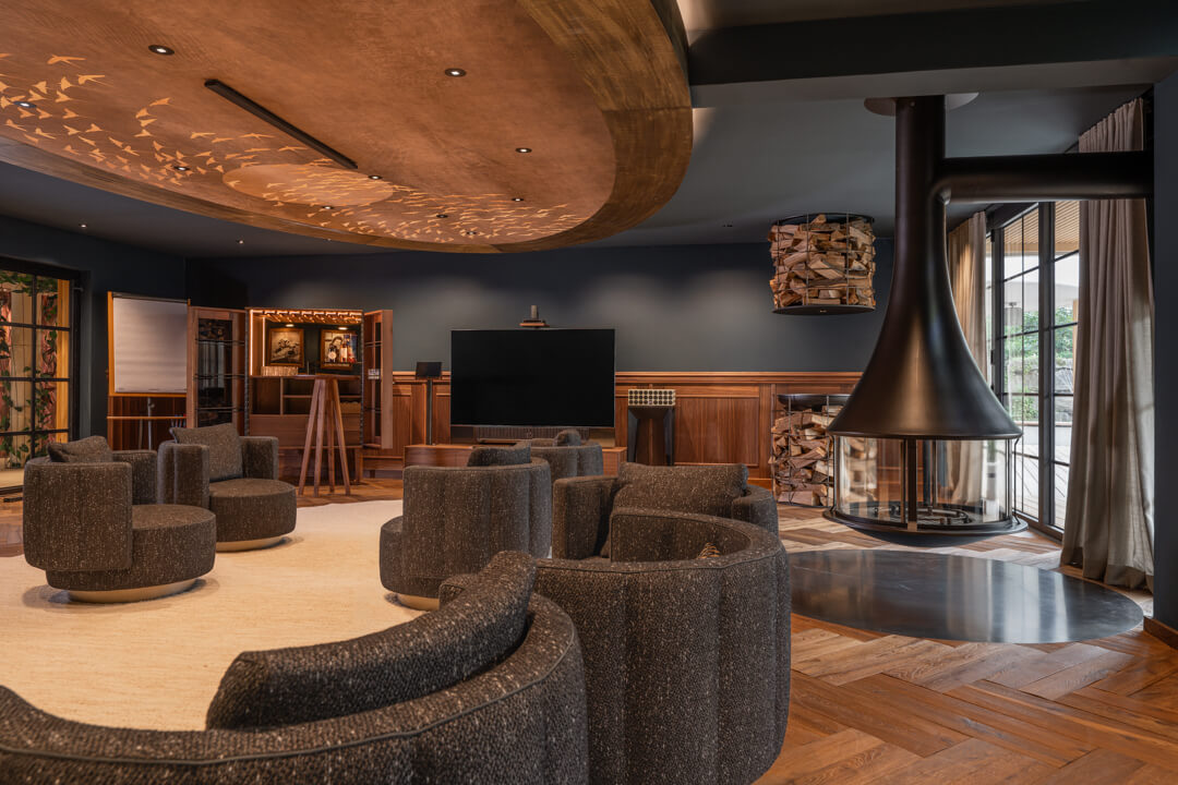 Fireplace room with dark interior, wood paneling, and herringbone floor at Hotel Rössle. Light wooden carpet and displayed black and white portraits. Tv display furniture. Illuminated wooden ceiling centerpiece.