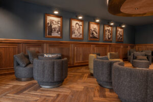 Dark interior, wood paneling, and herringbone floor. displayed black and white portraits. Cozy grey chairs.