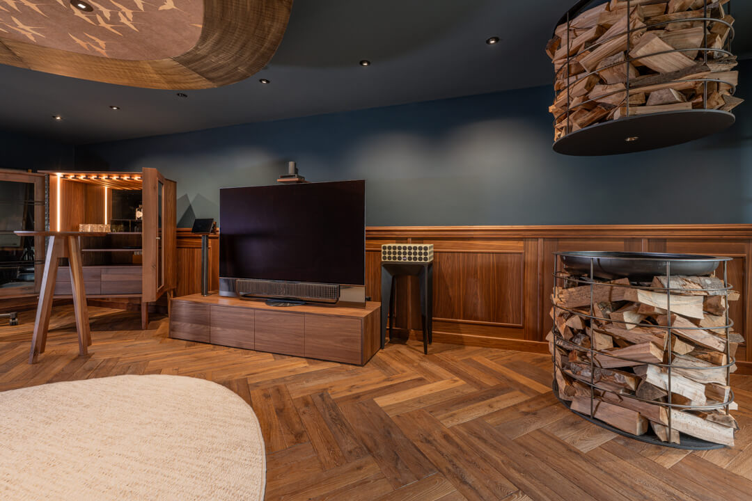 Dark interior green collered room, wood paneling, and herringbone flooring. Walnut Tv furniture. Champagne display centerpiece with stacked wood desig.