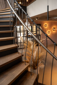 Oak staircase with sculptural steel railing. Decorative wall lighting fixture. Black loft doors