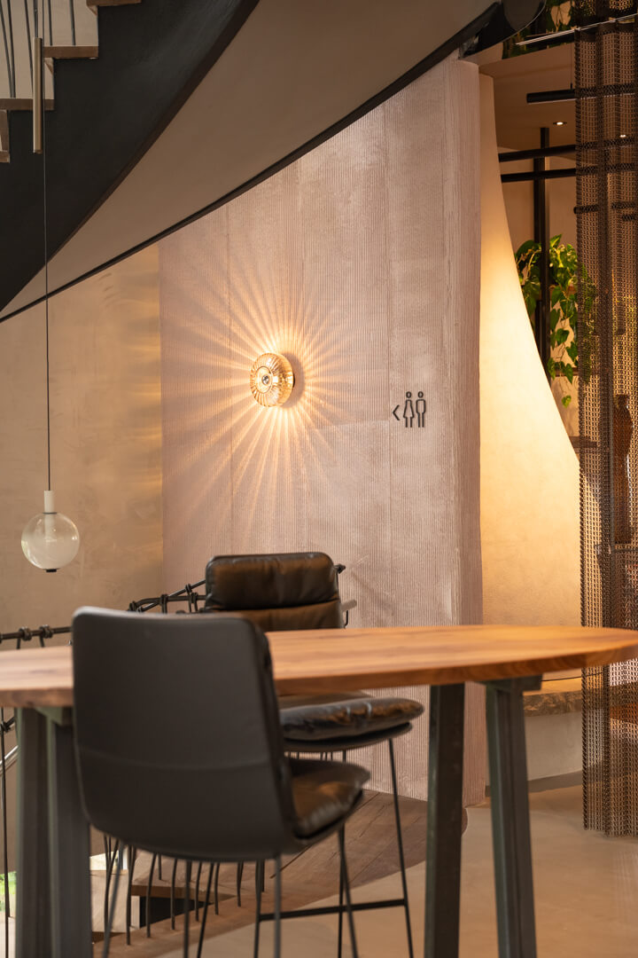 Structured light pink wall with a design wall lamp, walnut bar table with steel legs, and leather chairs.