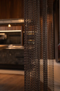 Bronze metal curtain serving as a room divider in an interior space.