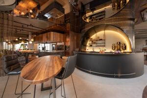 Warm walnut table, luxury grand kitchen with large stone island and wooden range hood, an imposing hotel bar with illuminated steel construction. 7,5 meter long oak table.
