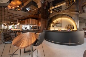 Warm walnut table, luxury grand kitchen with large stone island and wooden range hood, an imposing hotel bar with illuminated steel construction. 7,5 meter long oak table.
