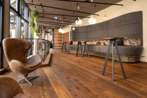 Dynamically designed foyer with a long grey design bench, steel railing, dark wooden flooring, and light brown leather chairs.