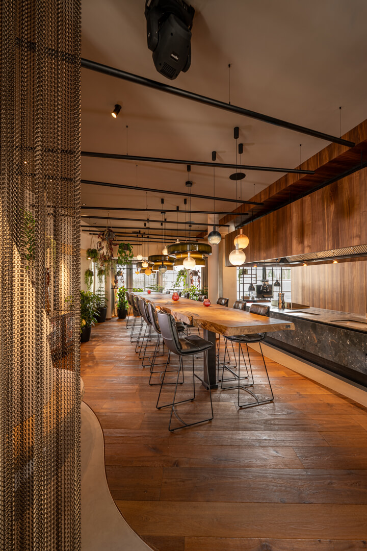 7.5-meter oak table with dynamic natural edge. Bar chairs and metal curtain.