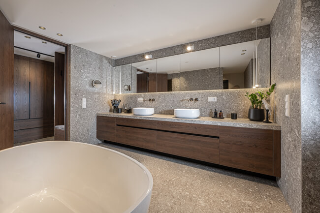Bathroom with matte, textured grey stone, dark oak furniture, and a walk-in closet in matching tones.